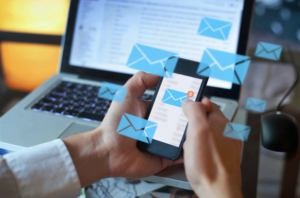 pair of hands holding a phone in front of a laptop with email icons surrounding the phone
