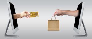 hands emerging from two computers, one holding a bag, the other holding a credit card.