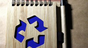 blue recycle icon on a the cover of a spiral notebook next to a pen